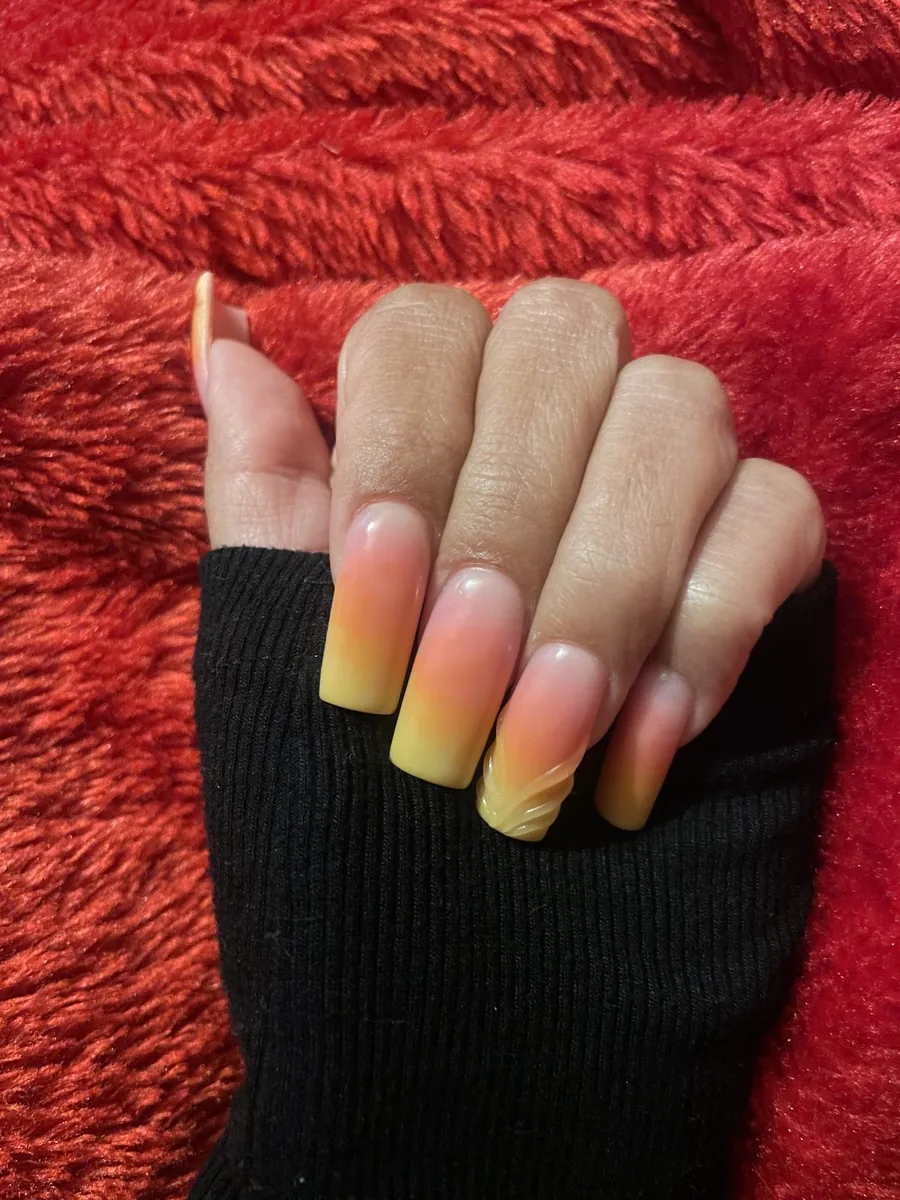 Peach and yellow ombre nails on red fabric, shot with the thumb in frame