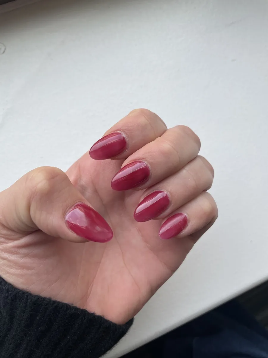 Short almond nails in a glossy deep cherry red against a plain white wall