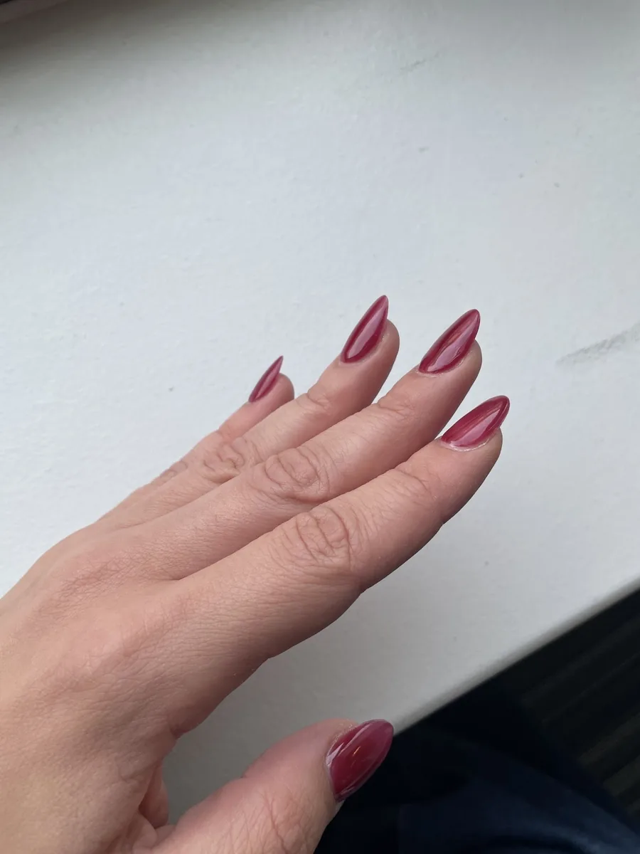 Side view of a deep red almond manicure showing the curve of the nail
