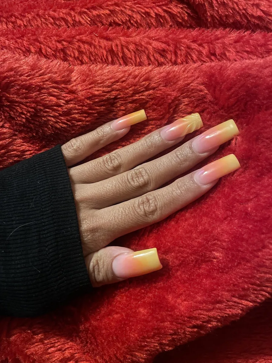 A hand laid flat showing long yellow ombre nail extensions, photographed from above on red fabric
