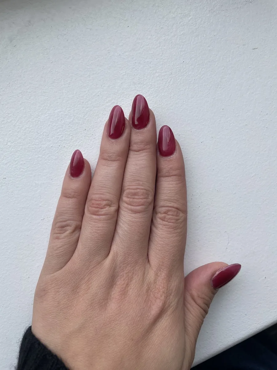 A hand held flat against a white wall showing a glossy deep cherry red almond manicure